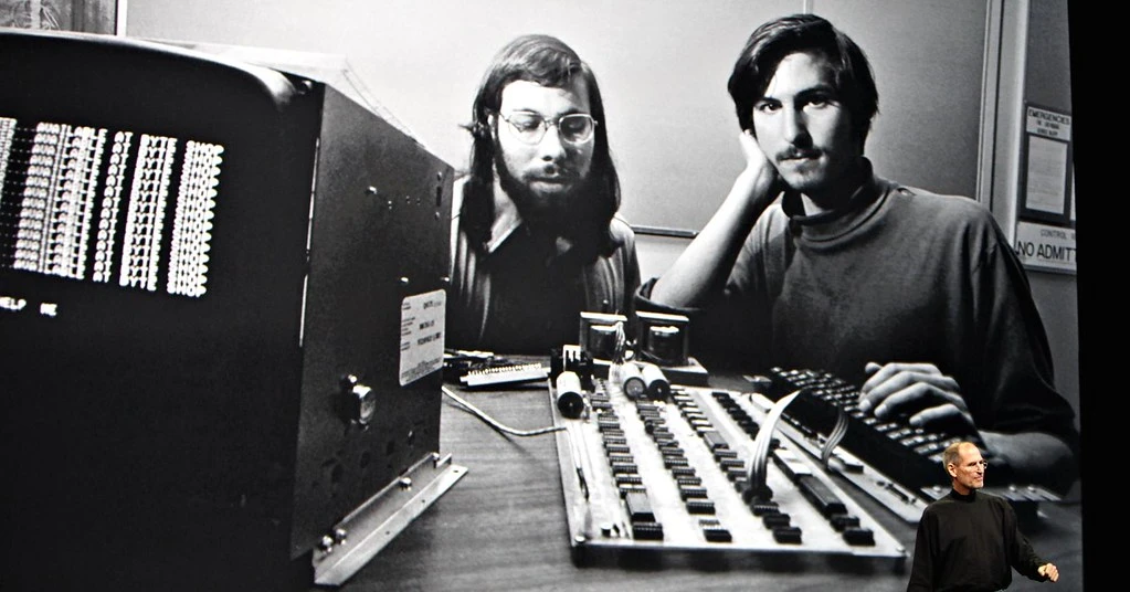 Steve Jobs az Apple 2010-es sajtóeseményén. Háttérben a vállalat másik kulcsfigurájával, Steve Wozniakkal készült közös képük 1976-ból. A régi fotón az Apple I számítógép látható.